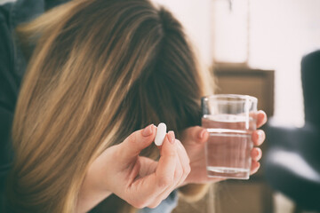 Sad young woman with pill and glass of water indoors, closeup. Toned for dramatic atmosphere
