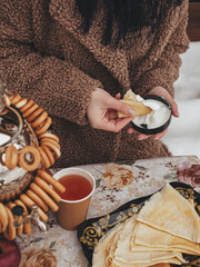 A girl eats pancakes with sour cream on a winter day and drinks tea from samovra. Carnival.