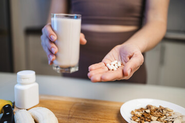 Athletic woman in sportswear holding a glass with a protein drink, milkshake, or smoothie and white amino acid capsules or vitamins in her hand