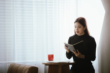 A young woman is relaxing in a cozy coffee shop, smiling as she sips her coffee. She uses her...