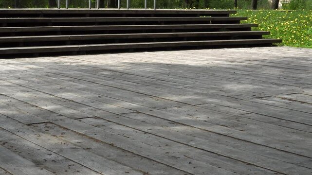 A wooden outdoor terrace with multiple steps leads up to it, surrounded by greenery and dandelions. This exemplifies the use of natural materials in urban landscape design.