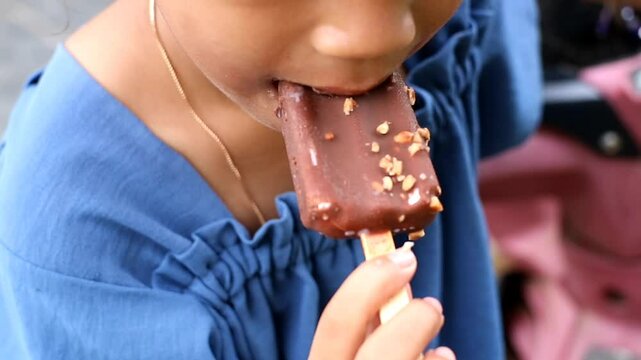 A little girl eats chocolate-covered ice cream and looks like she is enjoying it