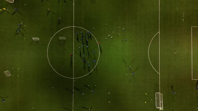 football training on an illuminated stadium in the evening. children and adults in jerseys run and exercise in circular training. small and large goals. view from above. the surroundings are dark