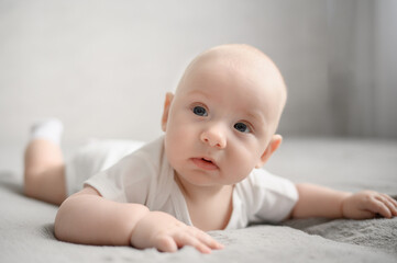Happy baby lying in crib on tummy, awake and looking around. Portrait of playful and energetic baby. Concept of strengthening muscles, preventing infant colic.