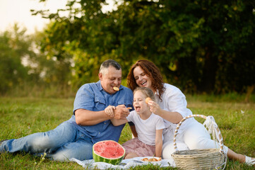 Lovely family enjoying picnic in park, sitting on grass eating delicious cookies. Family weekend, picnic, eating outside. Mom, dad and daughter enjoy spending time outside