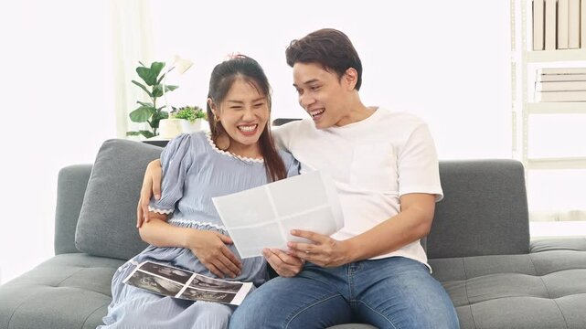 Happy pregnant husband and wife enjoy a relaxing day at home looking at the photo of their baby waiting for the birth with hope : Pregnant married couple excited about X-ray photo unborn son.