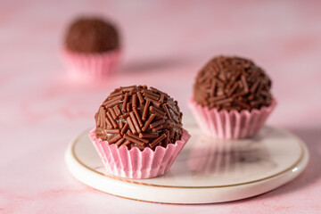  brigadeiro em forminhas de papel rosa sob um pratinho de mármore em um fundo rosa e dois brigadeiros desfocados atrás 