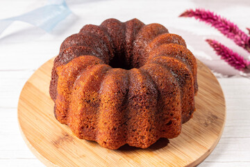 bolo caseiro mesclado em uma tábua de madeira, sob uma mesa de madeira clara, ao lado com uma flor seca e uma fita azul © Marina
