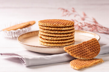 stroopwafel de caramelo sob um prato de ceramica em uma mesa de madeira clara com uma flor seca rosa e um pano cinza

