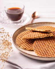 stroopwafel de caramelo sob um prato em uma mesa de madeira clara com uma xicara de café e uma...