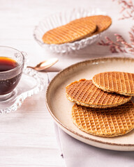 stroopwafel de caramelo sob um prato em uma mesa de madeira clara com uma xicara de café e uma flor seca