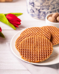 stroopwafel de caramelo em uma mesa de madeira clara com tulipas vermelhas e uma lata com desenhos...