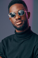 Obraz premium Stylish young Black man wearing sunglasses and a turtleneck sweater, showcasing confidence and modern fashion against a colorful background