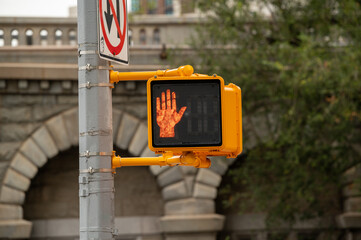 Prohibiting signal of pedestrian traffic lights. In a bustling city environment, a pedestrian traffic light shows a raised hand.