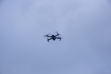Black quadcopter drone flies in gray winter sky. Propellers are blurred in motion as it hovers steadily in air.