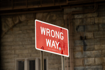 Traffic sign indicating wrong way near urban area, warning drivers of incorrect direction, captured during daylight hours with surrounding brick structure