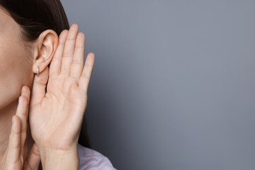 Woman showing hand to ear gesture on grey background, closeup. Space for text