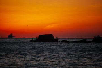 작은 섬의 낚시꾼 너머로 붉은 태양이 떠오르는 바다 일출 풍경