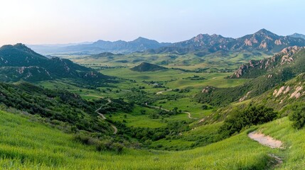 Fototapeta premium Scenic valley landscape at dawn, winding roads, green hills, mountains, background peaceful sky. Use travel brochures