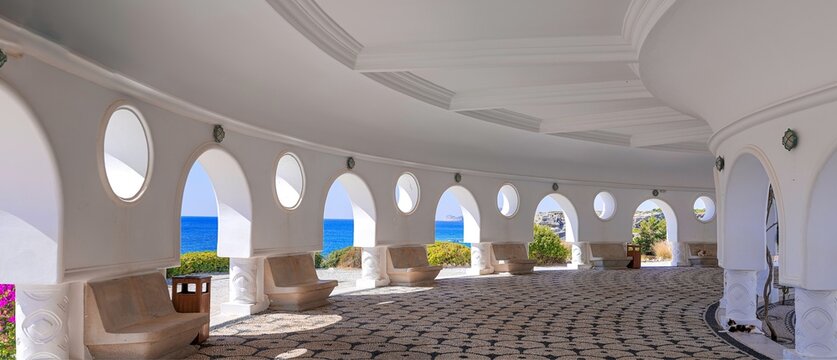 Architectural structure with arches and circular windows at Kallithea Springs, Rhodes, Greece. The open side provides sea views and surrounding greenery, with mosaic floors and stone benches.
