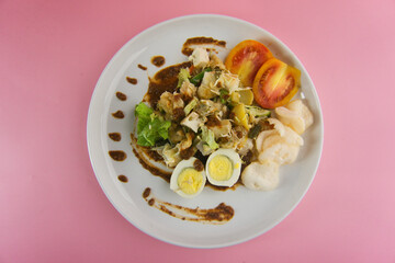 Colorful Gado-Gado Salad Dish with Vegetables, Boiled Eggs and Peanut Sauce on Pink Background