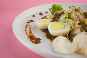 Colorful Gado-Gado Salad Dish with Vegetables, Boiled Eggs and Peanut Sauce on Pink Background