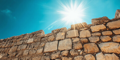 Close-up of ancient stone wall with weathered texture under bright sunlight, symbolizing history, resilience, and architectural heritage against a vibrant blue sky.