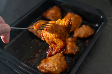 Chicken thighs, fried in a roasting tray, as they came out of the oven. Hand with fork is picking a piece up. Selective focus.