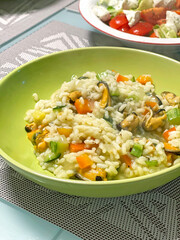 Risotto with vegetables and mussels on green plate at home. Vegetables and seafood. National cuisine of Europe. 