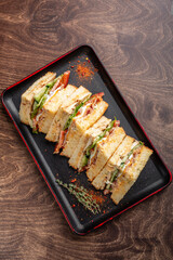 A delicious sandwich cut into pieces, featuring layers of lettuce, tomato, and creamy dressing, arranged neatly on a black tray. Perfect for a tasty lunch or snack.