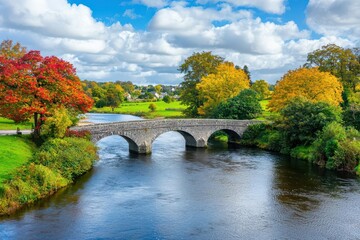 Fototapeta premium A quaint stone bridge crossing a gently flowing river surrounded by greenery