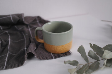 an empty green mug with a towel on a white table against a background of eucalyptus branches