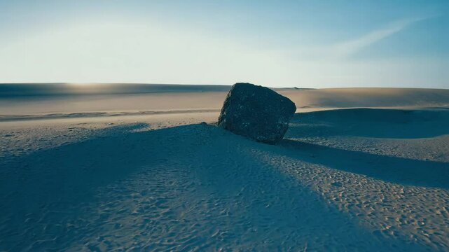 Timelapse side light video establishing scene of a rock in the desert with shadows lengthening on the sand