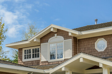 Top of grey stucco luxury house with shingle roof, red and yellow trees and nice windows in Spring in Vancouver, Canada, North America.