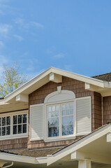 Top of grey stucco luxury house with shingle roof, red and yellow trees and nice windows in Spring in Vancouver, Canada, North America.