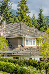 Top of grey stucco luxury house with shingle roof, red and yellow trees and nice windows in Spring in Vancouver, Canada, North America.