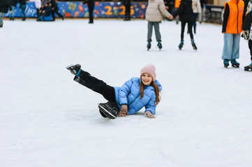 Beautiful smiling girl, child teenager slipped on skates lies on ice rink outdoors after fall. Photography, portrait, hobby and sport concept.