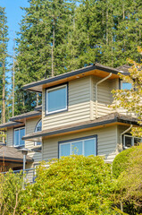 Top of grey stucco luxury house with shingle roof, red and yellow trees and nice windows in Spring in Vancouver, Canada, North America.