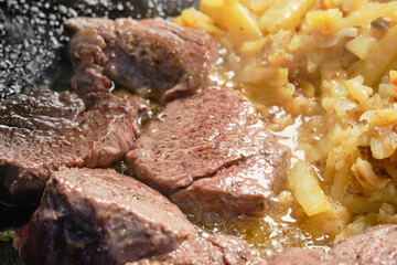 Searing, frying beef meat roast and potatoes in cast iron skillet , shallow depth of  field.