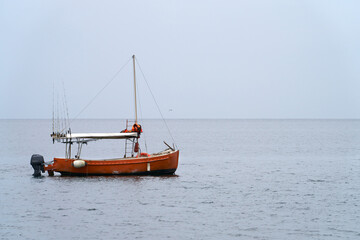Fototapeta premium Fishing tourism. Sea fishing at a distance from the shore. A lone motorboat with a set of fishing rods on board is anchored in a sea bay. Copy space.