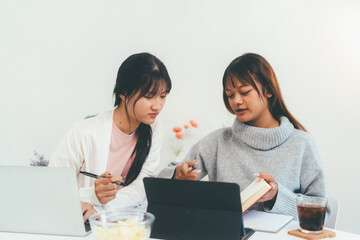 Female higher education student using laptop and studying book in home, Online learning.