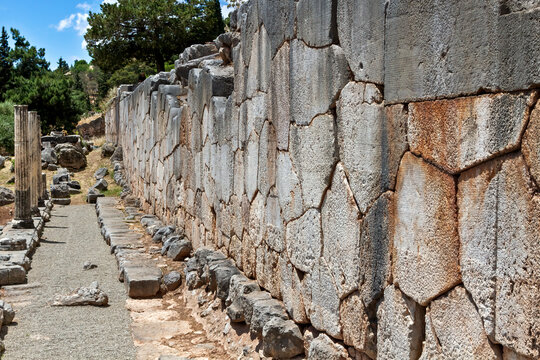 Close-up view of an ancient stone wall in Delphi, Greece, featuring polygonal masonry with weathered textures, surrounded by scattered ruins and lush