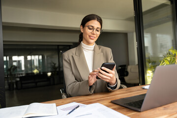 Focused Latin Hispanic female businesswoman holding smartphone sitting at desk in office. Successful middle age business woman manager ceo using cell phone mobile pc for online working. Copy space