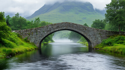 Fototapeta premium medieval stone bridge crossing over a calm river, surrounded by lush greenery and misty mountains in the background,