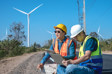 Male Japanese wind turbine engineer working on laptop in wind power plant with female electrician coworker 