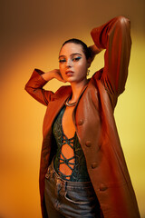Fototapeta premium A young woman showcases her exquisite makeup and trendy snake print attire under warm studio lights.
