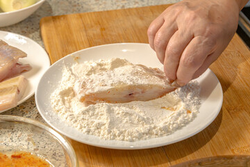 Chef dips pieces of fresh fish in flour before further frying in a frying pan