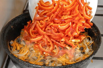 Chef adds sliced ​​red peppers to the fried vegetables in the frying pan. Close-up