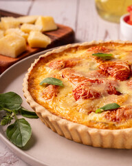 Quiche de tomate com queijo e manjericão, elementos como azeite, tomate e manjericão ao redor da cena