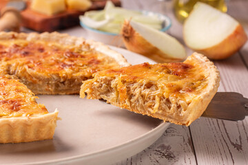 quiche de cebola caramelizada com elementos ao redor como azeite, queijo parmesão e cebola fatiada 
